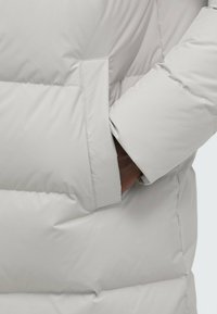 Light gray puffer jacket with a textured, quilted pattern, featuring a side pocket and a slightly padded sleeve for warmth.