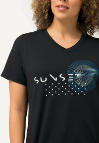 Musta V-kaulus T-paita, jossa on valkoinen teksti "AURINGONLASKU" ja sinivihreä aaltoileva kuvio pienten valkoisten neliöiden kanssa tekstin alla.