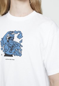 Bílý bavlněný tričko s modrou grafikou svalnatého muže, který stříká z plechovky, s textem "trochu příliš doslovné" pod designem.