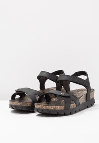 Sorte sandaler med to justerbare stropper, korklignende såle og strukturert gummisåle. Merkbar design inkluderer blomstermønstre på innersålen.