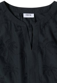 Haut noir avec un décolleté fendu et de subtils motifs brodés de palmiers, avec une étiquette blanche portant le nom de la marque "Cecil."