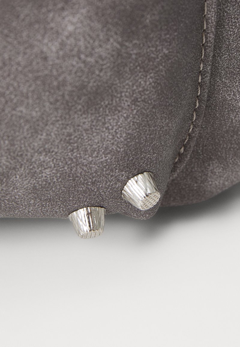 Bolso de ante gris con una textura suave, que presenta dos patas en tono plateado en la base. Detalles de costura a lo largo de los bordes.