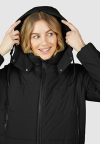 Schwarze Daunenjacke mit hohem Kragen und verstellbarer Kapuze. Mit Reißverschluss-Taschen und vertikalen Nähten für Textur.