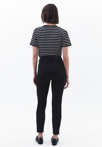 Jeans negros de tiro alto con un ajuste slim, combinados con una camiseta a rayas en blanco y negro. El modelo se muestra de espaldas, con mangas cortas.