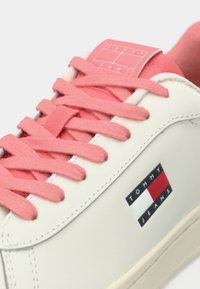 Λευκό αθλητικό παπούτσι με ροζ κορδόνια και πλακέτα λογότυπου· ομαλή υφή με χαμηλή κατασκευή και διακριτικές λεπτομέρειες στο πλάι. Λαστιχένια σόλα.