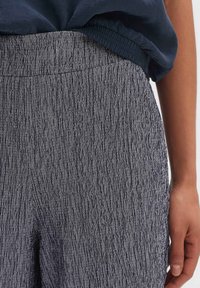 Texturerade, mörkblå byxor med en mjuk, elastisk midja. Har ett vertikalt ribbat mönster och en rak passform som visar subtila detaljer.