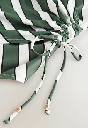 Tessuto a righe verdi e bianche con coulisse. Presenta una texture arricciata e dettagli in metallo alle estremità della coulisse. Materiale morbido e leggero.