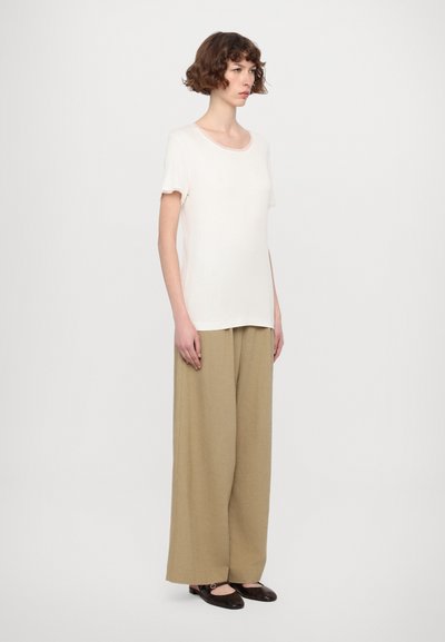 Light beige short-sleeved top paired with wide tan pants. Model wears dark brown flat shoes. The background is plain and white.