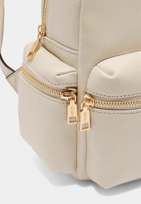Helle beige Tasche aus strukturiertem Leder. Mit goldenen Reißverschlüssen und Beschlägen, zwei Reißverschlussfächern und glatten Kanten.