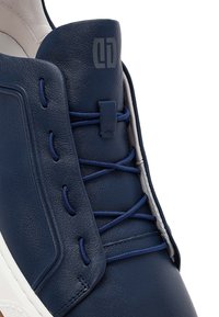 Granatowy skórzany sneaker z elastycznymi sznurowadłami, boczną skórzaną wstawką oraz szarym logo marki na języku, wyposażony w białą podeszwę.