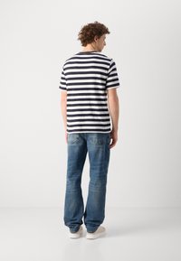 Gestreiftes Baumwoll-T-Shirt in Marineblau und Weiß mit kurzen Ärmeln, kombiniert mit hellblauen Jeans; Modell von hinten gesehen.