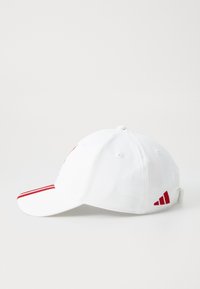 Hvidt stof baseballkappe med røde striber på skyggen og et lille rødt logo på siden, vist mod en simpel hvid baggrund.