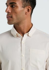 Licht crèmekleurig overhemd met knopen, gemaakt van een textuurstof, met een kraag, een vo pocket met logo en witte knopen.