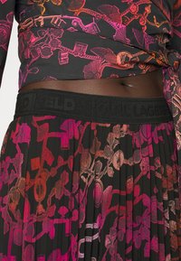 Czarna plisowana spódnica z kolorowymi wzorami łańcuchów i zawieszek. Posiada czarną elastyczną talię z logo "KARL LAGERFELD".