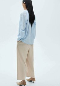 Blusa azzurra a maniche lunghe con scollo arricciato, abbinata a pantaloni beige larghi e scarpe slip-on color nude. Tessuto dalla consistenza liscia.