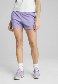 Lavender athletic shorts with vertical ribbed texture, elastic waistband, and a white logo on the side. Paired with silver and purple sneakers.