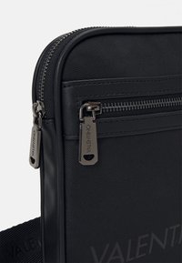 Černá ramenní taška s texturovaným vnějším povrchem, dvěma zipovými přihrádkami a kovovými detaily s brandingem "Valentino".
