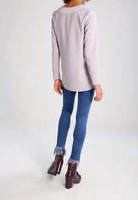 Maglietta grigia a maniche lunghe abbinata a jeans skinny blu con orli sfilacciati, completata da stivaletti alla caviglia bordeaux scuro con tacco.