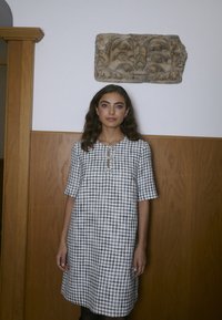 Karo obleko v črno-beli barvi s kratkimi rokavi, okroglim izrezom in detajlom gumbka v obliki ključavnice spredaj. Strukturirano blago.