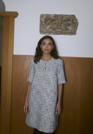 Černo-bílá kostkovaná šaty s krátkými rukávy, kulatým výstřihem a detaily na knoflíček ve tvaru klíčové dírky vpředu. Strukturovaná tkanina.