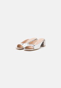 Scarpe con tacco blocco aperte davanti in argento con finitura lucida, dotate di punta arrotondata e interno liscio. Design semplice e minimalista.