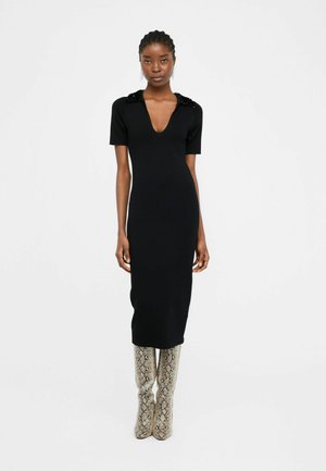 Black knee-length dress with a V-neck and short sleeves, featuring embellished shoulders. Paired with high, textured snake-print boots.