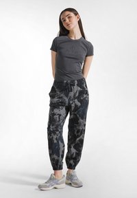 Szara dopasowana koszulka z logo, zestawiona z czarno-szarymi wzorzystymi dresami. Look dopełniają sportowe buty z szaro-fioletowymi akcentami.