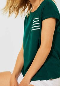 Grön kortärmad t-shirt med randig fickdetalj. Mjukt tyg med avslappnad passform, med rund halsringning och synliga sömmar.