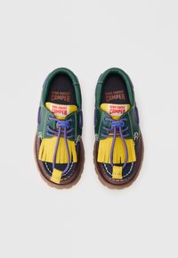 Flerfargede sneakers med et grønt og marineblått skinnøvre, gule duskler, lilla snørebånd og en brun gummisål.