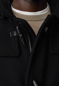 Manteau en laine noire avec une fermeture éclair à l'avant, des accents en tissu, et un col rond beige chaud en dessous. Comprend une capuche et un matériau texturé.