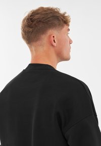 Svart sweatshirt med rund halsringning och ribbad krage. Tjockt, mjukt tyg med en avslappnad design. Har sänkta axlar och en enkel struktur.