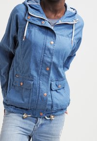 Blå denimjacka med huva, tryckknappar, två framfickor och dragsnodd i nederkant. Mjuk textur med kontrasterande detaljer.