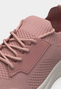 Κοντινό πλάνο ροζ πλεκτού αθλητικού παπουτσιού με κορδόνια ίδιου χρώματος, υφή σχεδίων και λευκή σόλα.