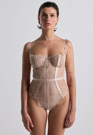 Body in pizzo color nudo. Presenta coppe con stecche, spalline in satin, dettagli in pizzo e orlo a zig zag. Design strutturato con una silhouette aderente.