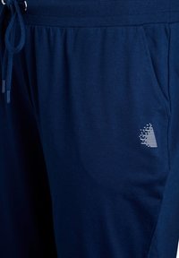 Marineblauwe sweatpants van zachte stof, met een trekkoord in de taille, elastische boorden en een wit logo ontwerp aan de zijkant.
