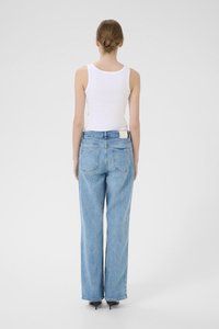 Lyseblå høyt midje jeans med vide ben, fire lommer og en merkelapp på baksiden. Modellen har på seg en hvit tettsittende tank top.