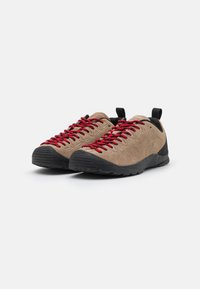 Chaussures d'escalade beige avec des semelles noires et des lacets rouges, dotées d'un design profil bas et de boucles au talon pour un enfilage facile.