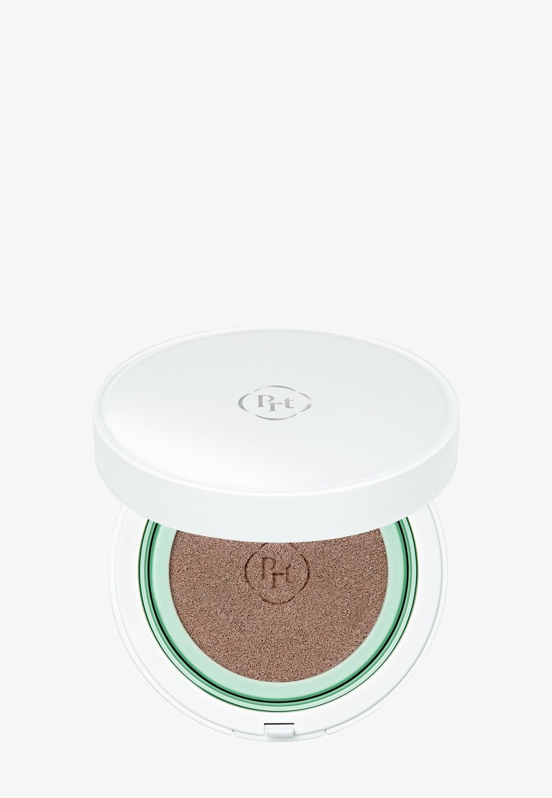 Boîtier compact blanc pour fond de teint cushion avec une éponge beige et un anneau intérieur vert, marqué d'un logo circulaire dessus et à l'intérieur.
