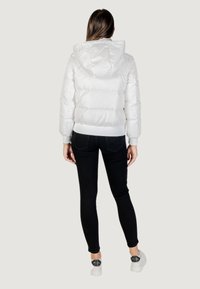 Giacca trapuntata bianca con cappuccio, caratterizzata da un design a quadri e polsini a coste. Abbinata a leggins neri e sneaker bianche.