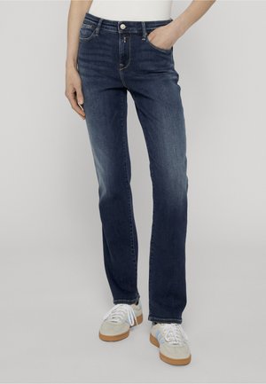 Person iført mørkeblå jeans med lige ben og forlommer, kombineret med hvide sneakers med lyseblå striber og gummisåler.