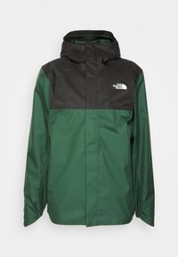 Veste résistante à l'eau avec une partie supérieure noire et une partie inférieure verte, dotée d'une capuche et d'une fermeture éclair. Logo sur la poitrine.