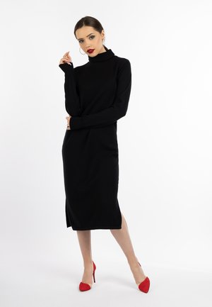 Vestito nero in maglia a maniche lunghe con colletto alto e spacchi laterali. Scarpe rosse con tacco alto completano il design elegante. Tessuto liscio, accenti minimi.