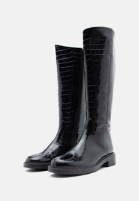 Bocanci de piele lacuită negri, până la genunchi, cu un model de piele de crocodil, vârf rotund și toc mic. Au o fermoar pe lateral pentru închidere.