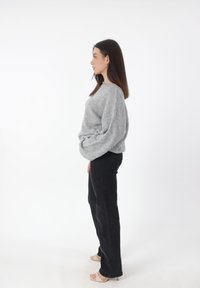Grijze oversized gebreide trui met lange mouwen, gecombineerd met zwarte rechte broek en beige open teen hakken. Goede textuur, casual pasvorm.