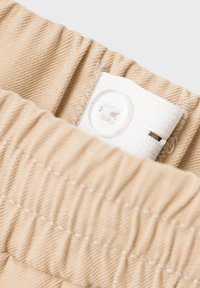 Beige tyg med en strukturerad yta och elastiskt midjeband; har en vit knapp med en sydd flik fäst.