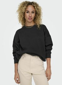 Svart oversized sweatshirt med ribbade ärmslut, rundad halsringning och mjukt material, ihop med ljusbeige hög midja byxor. Enkel guldkedja som accent.