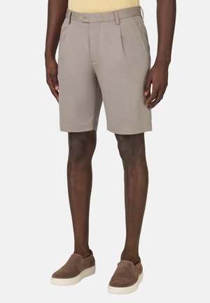 Pantaloni corti beige a pieghe con chiusura a bottone e tasche laterali, realizzati in tessuto morbido, con una vestibilità sartoriale e un orlo che arriva a metà coscia.