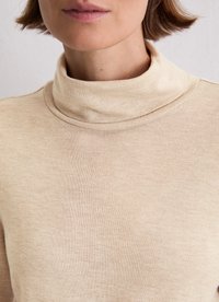 Beżowy sweter z golfem wykonany z miękkiego materiału, charakteryzujący się przytulnym, kołnierzykowym fasonem oraz gładką, teksturowaną powierzchnią.