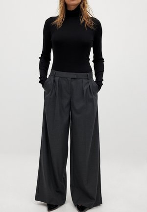 Zwarte geribbelde coltrui en grijze wijde pantalon met plooien, met een gladde textuur en zijzakken, gecombineerd met zwarte hakken.