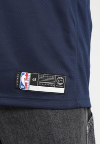 Maillot NBA en mesh bleu marine avec une étiquette noire. Comprend le logo NBA, la taille 48 et un détail NikeConnect. Le tissu a un motif texturé.